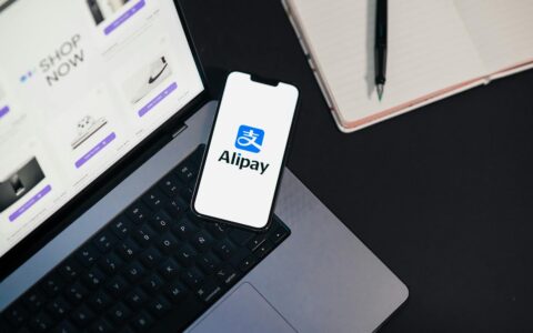 Smartphone displaying Alipay app on open laptop with online shopping site.